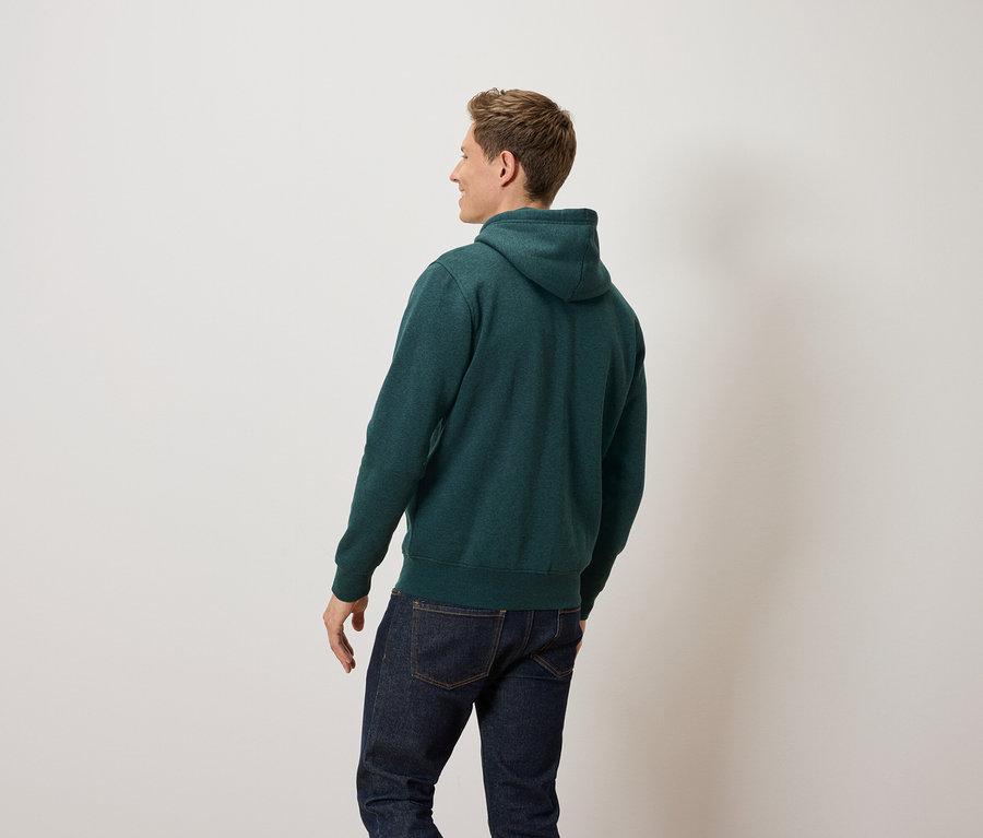 Un homme regarde vers la gauche et porte un sweat à capuche vert et un jean.