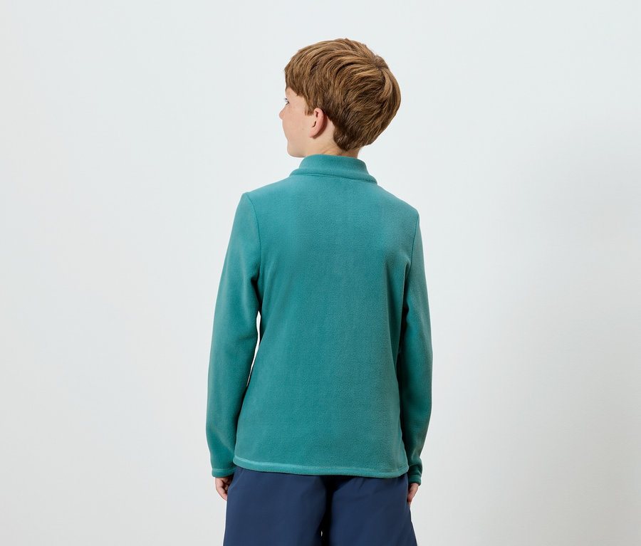 Vue de dos, une personne aux cheveux bruns courts portant un haut à manches longues bleu-vert et un short bleu marine.