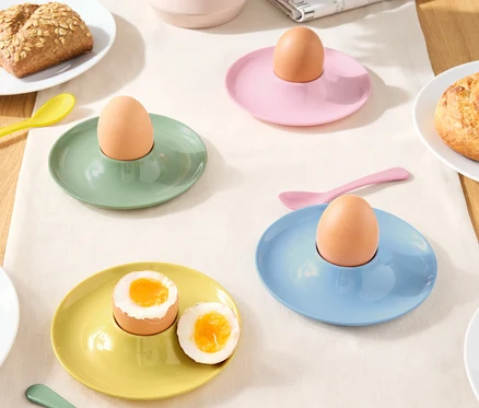 Coquetiers de différentes couleurs avec des œufs et des cuillères sur une nappe.