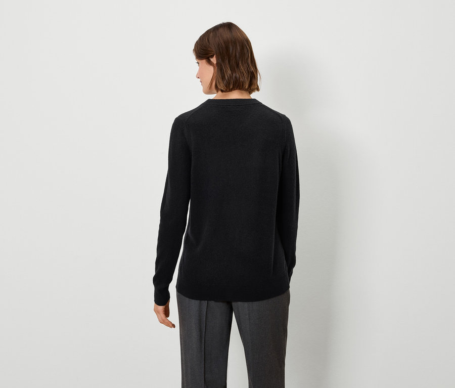 Une femme portant un pull noir et un pantalon gris, vue de dos.
