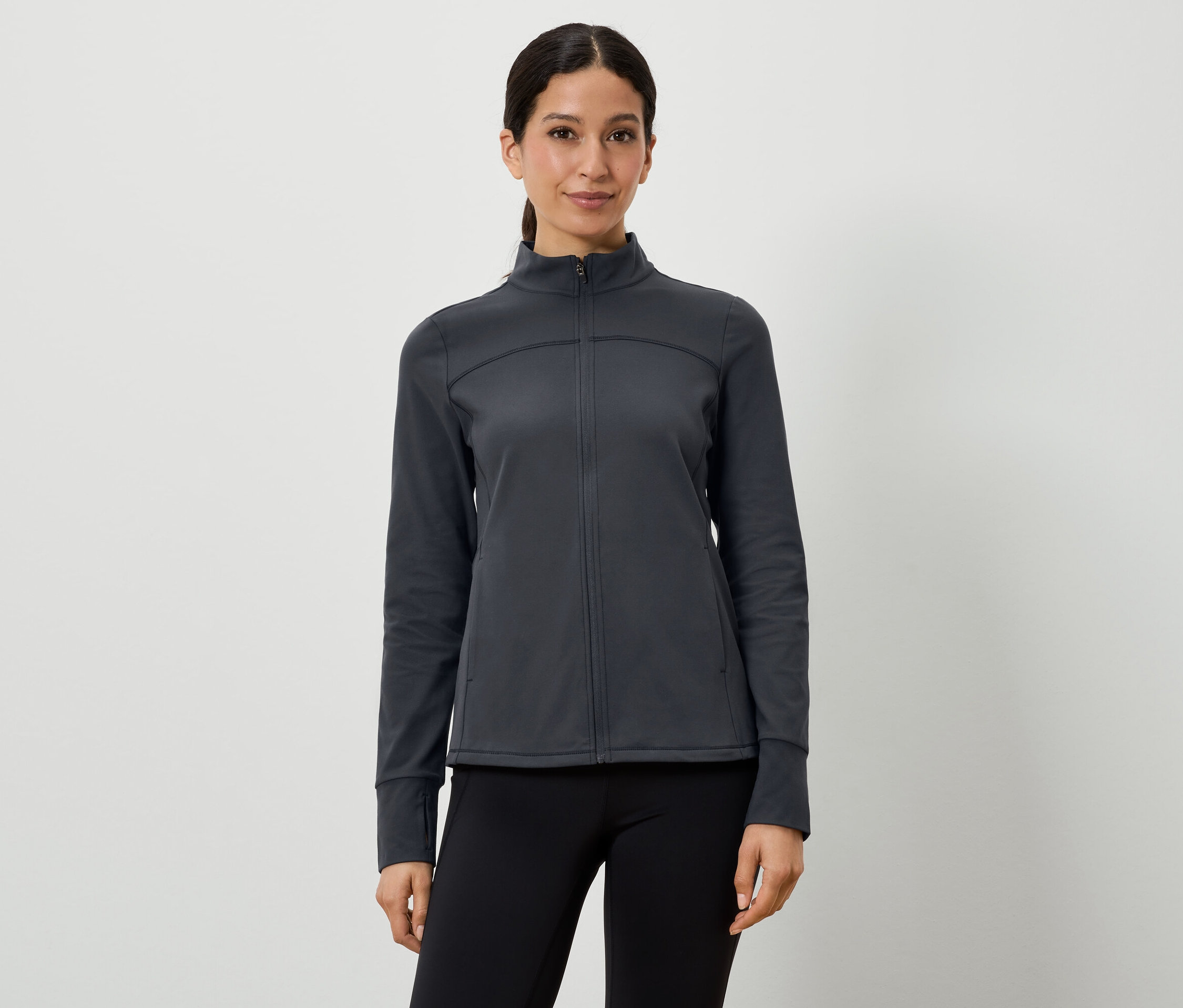 Une femme porte une veste de sport gris foncé et un legging noir.