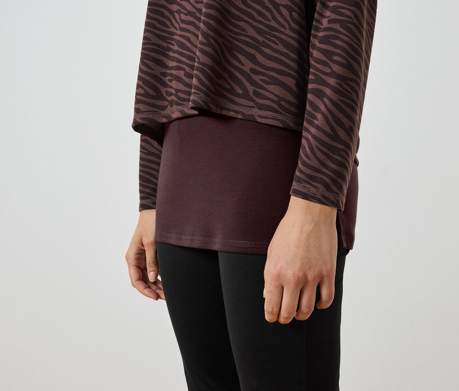 Gros plan d'une femme portant une tunique zébrée marron et noire, un haut bordeaux et un legging noir.