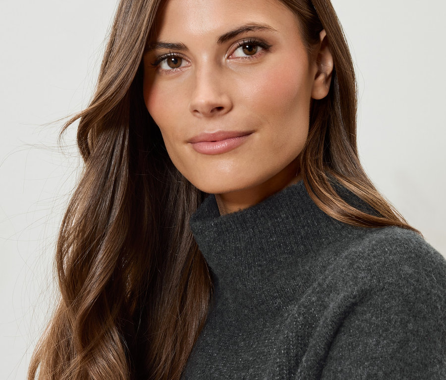 Portrait d'une femme aux cheveux bruns portant un pull à col roulé gris.