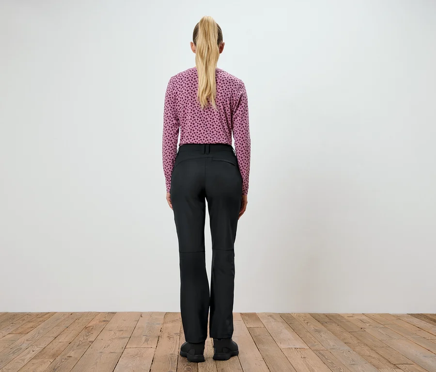 Une femme, vue de dos, porte un haut violet imprimé et un pantalon noir.