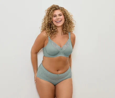 Femme souriante aux cheveux bouclés posant dans un soutien-gorge vert d'eau avec de la dentelle et une culotte assortie.