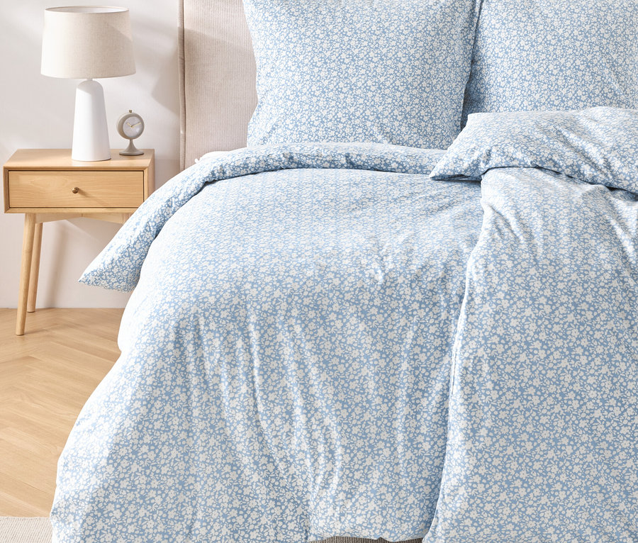 Gros plan d'un lit avec du linge de lit en jersey de taille standard avec un motif floral bleu et blanc.