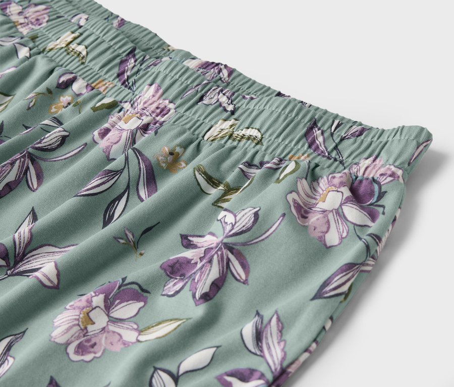 Détail d'un pantalon vert clair avec des fleurs violettes et une taille élastique.