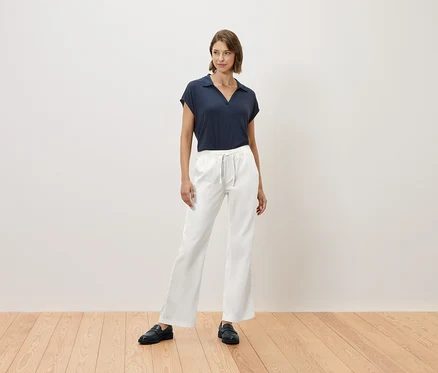 Une femme se tient sur un plancher en bois et porte un t-shirt bleu marine et un pantalon blanc.