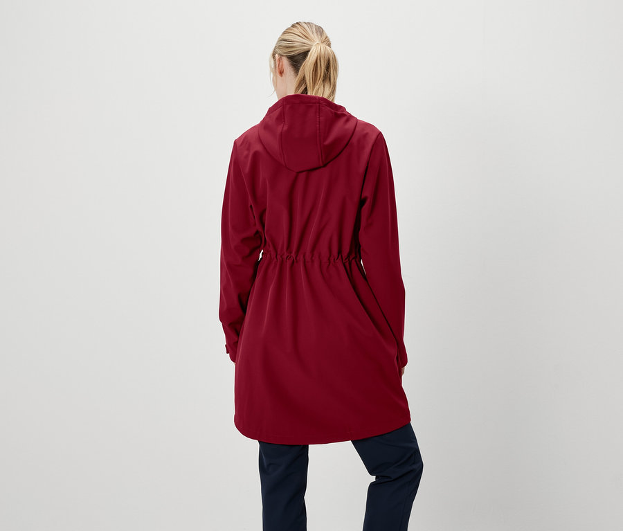 Une femme, dos à la caméra, porte une veste rouge à capuche et un pantalon bleu marine.