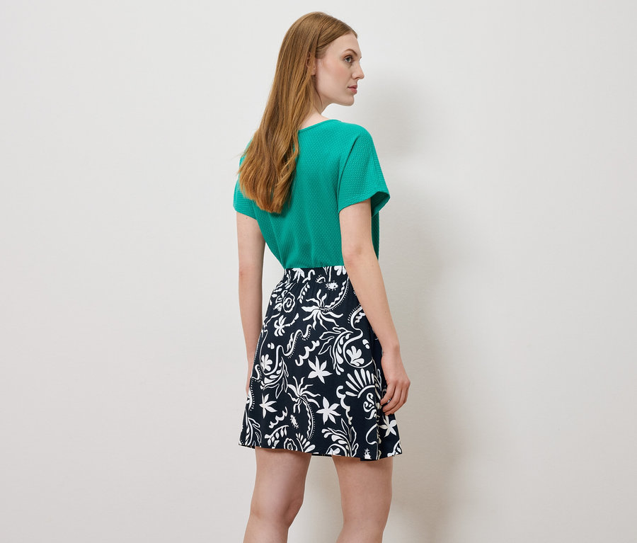 Femme vue de dos, portant un haut vert et une jupe à motifs.