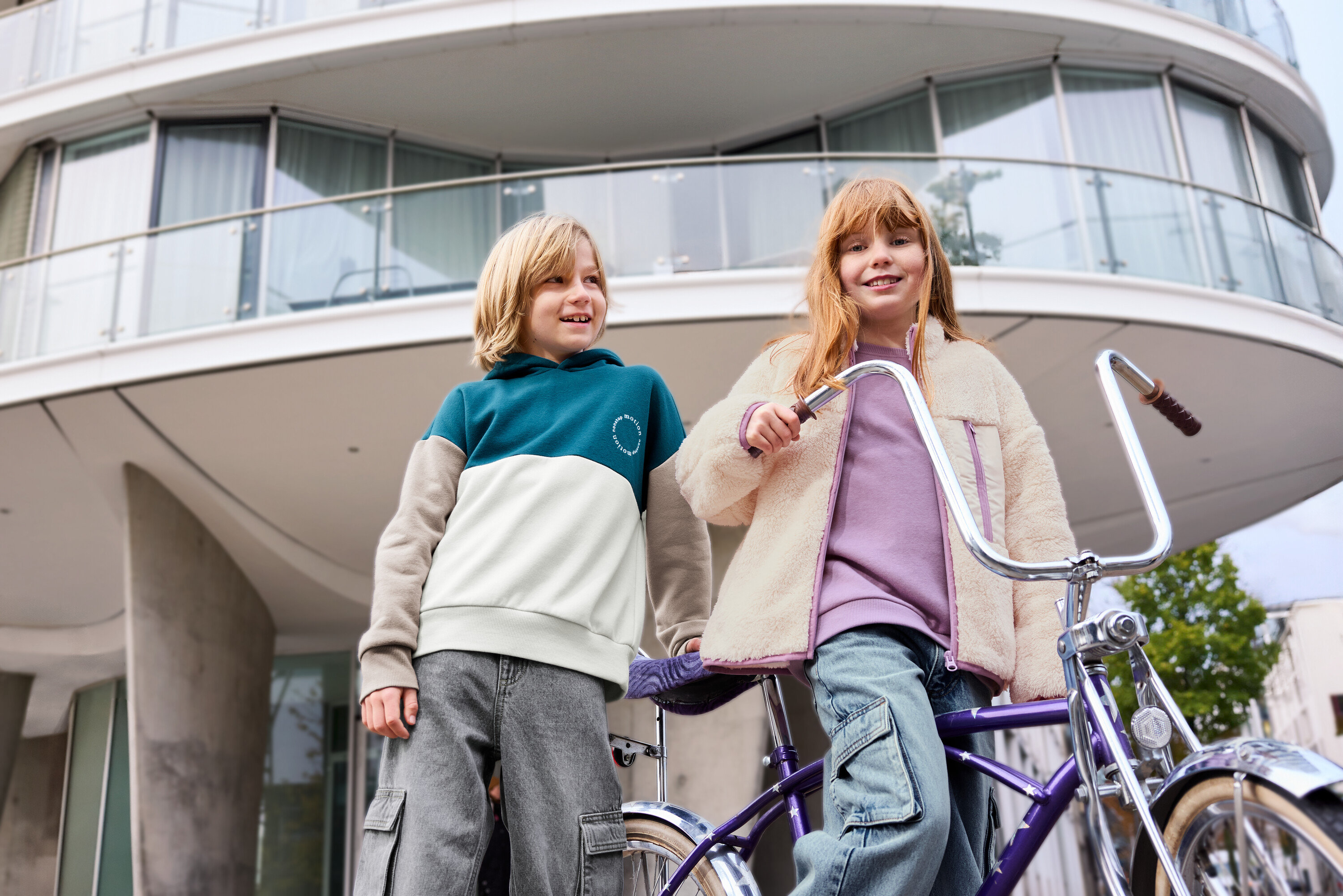 Deux enfants se tiennent devant un immeuble, un enfant porte un sweat-shirt pour enfant à intérieur gratté lavande.
