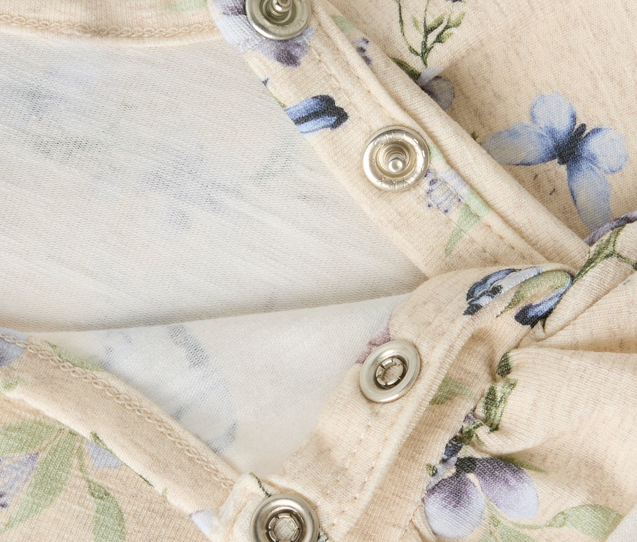 Gros plan sur une robe pour bébé NAME IT avec motif floral et boutons-pression.