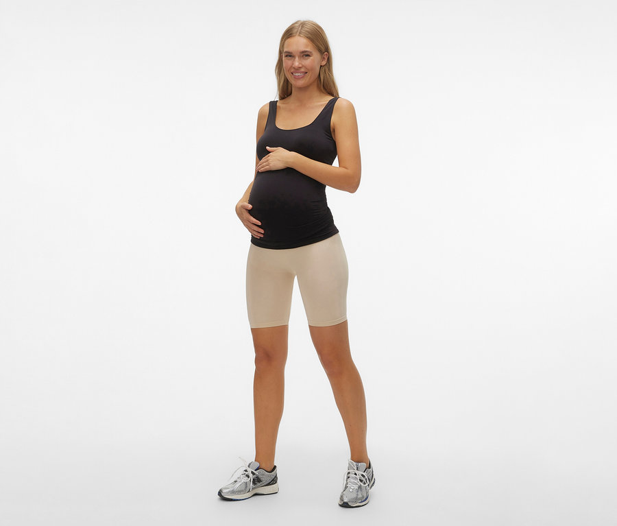 Une femme enceinte portant un débardeur noir et un Skinny Shorts MAMALICIOUS «	MLTIA JEANNE	» noir pose sur un fond blanc.