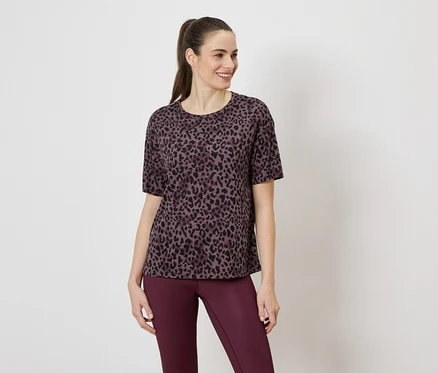 Une femme porte un t-shirt violet à motif léopard et un legging violet sur un fond blanc.