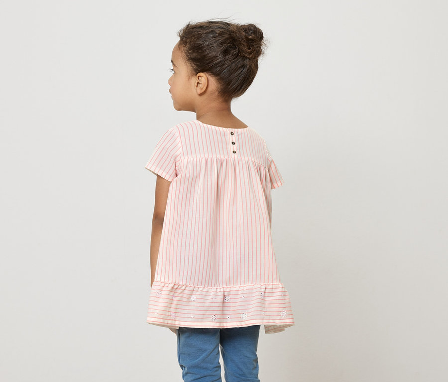 Une jeune fille, dos à la caméra, porte une robe rayée rose et blanche et un jean bleu.