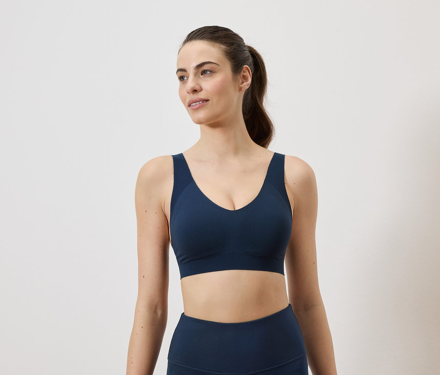 Une femme avec une queue de cheval porte un soutien-gorge de sport bleu marine et un legging sur fond blanc.