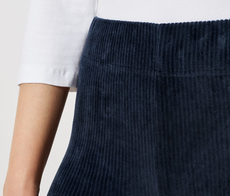Gros plan d'une personne portant un t-shirt blanc et une jupe en velours côtelé bleu marine.