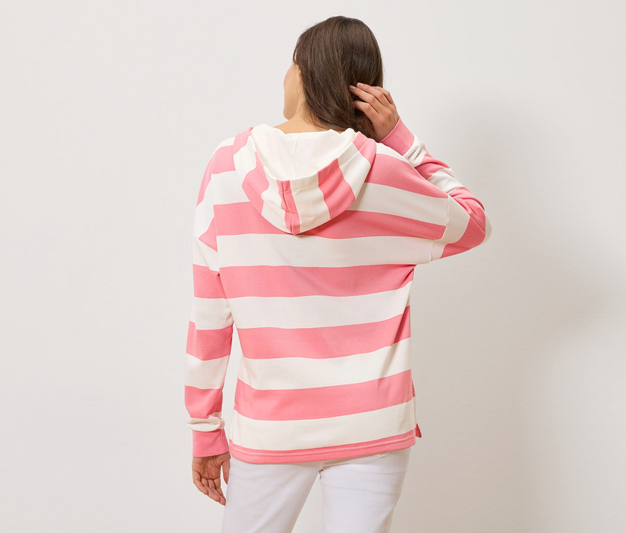Femme vue de dos, portant un sweat à capuche rayé rose et blanc et un pantalon blanc.