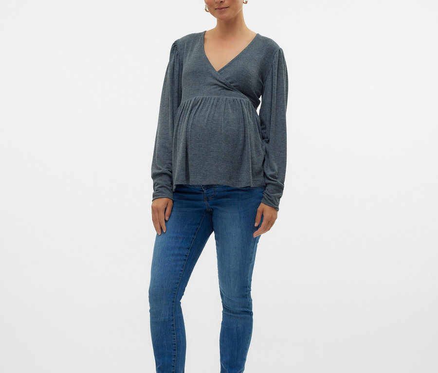 Femme enceinte portant un haut gris à manches longues, un jean bleu et des ballerines noires.