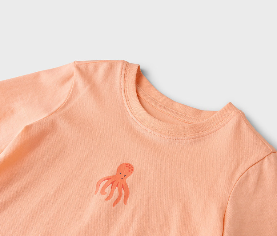 Gros plan d'un t-shirt couleur saumon avec un petit motif de poulpe.
