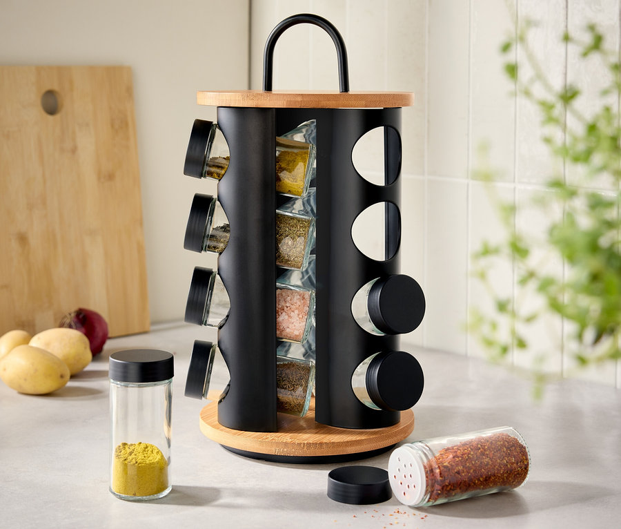 Sur un plan de travail de cuisine, un présentoir à épices rotatif en bois et métal avec des pots à épices remplis. Deux pots à épices sont posés à côté.