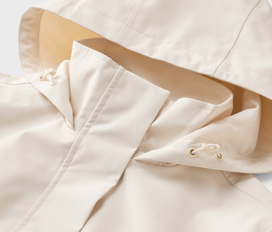 Gros plan d'un imperméable beige clair avec capuche. La capuche a un tissu intérieur jaune clair et des cordons de serrage.