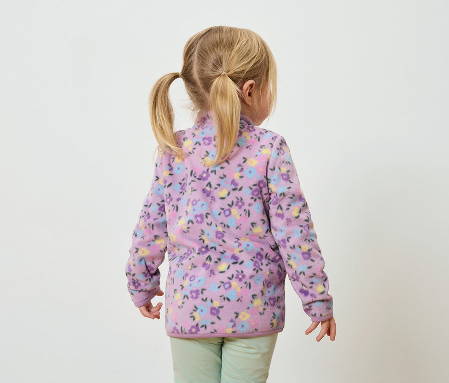 Vue de dos d'une petite fille avec des tresses blondes portant une veste polaire lilas à motifs floraux et un pantalon vert.