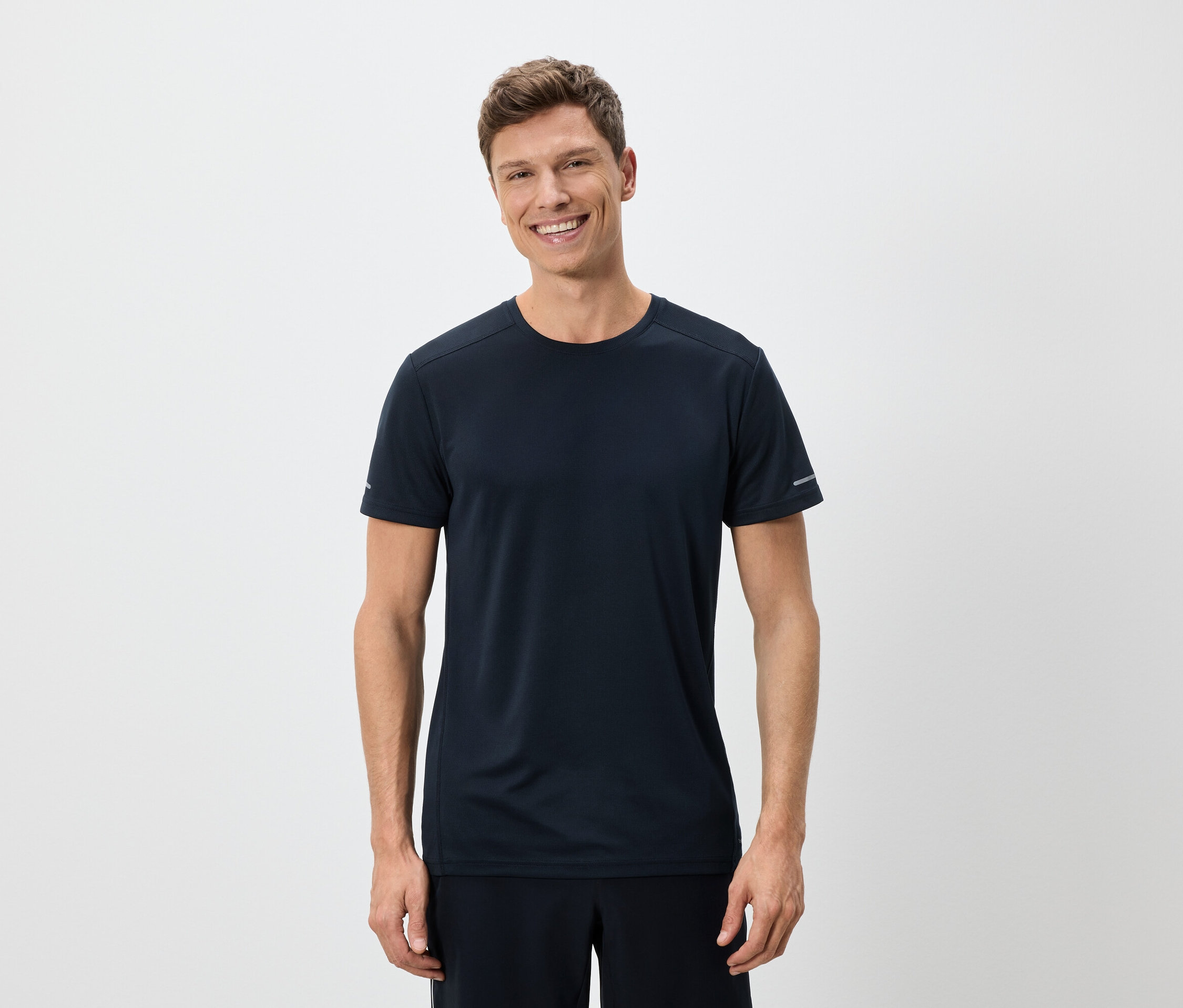 Un homme souriant portant un t-shirt bleu marine et un short sur un fond blanc.