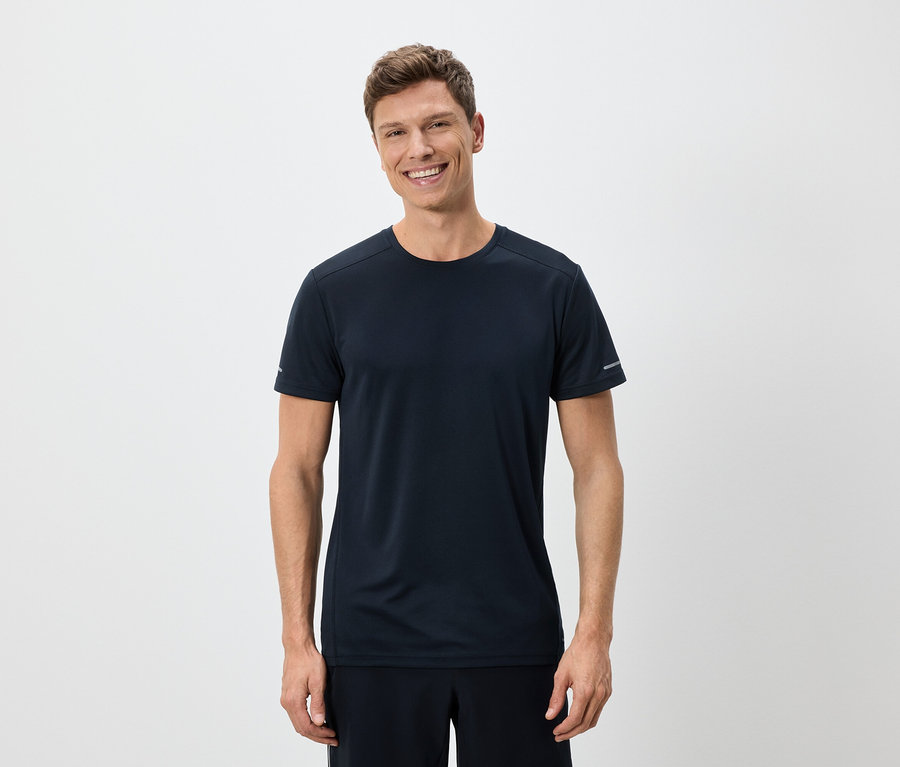 Un homme souriant portant un t-shirt bleu marine et un short sur un fond blanc.