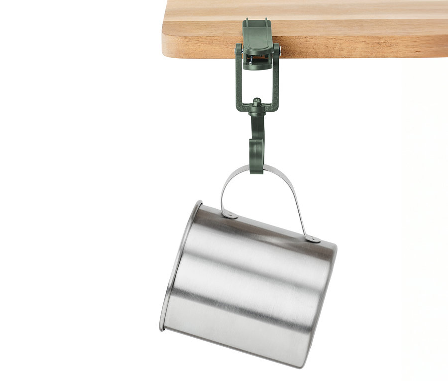 Une pince verte maintient une tasse argentée sur un plateau de table en bois.