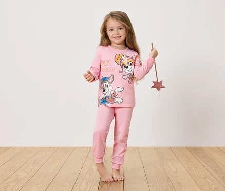 Une fille aux longs cheveux blonds porte un pyjama rose Pat' Patrouille et tient une baguette magique.