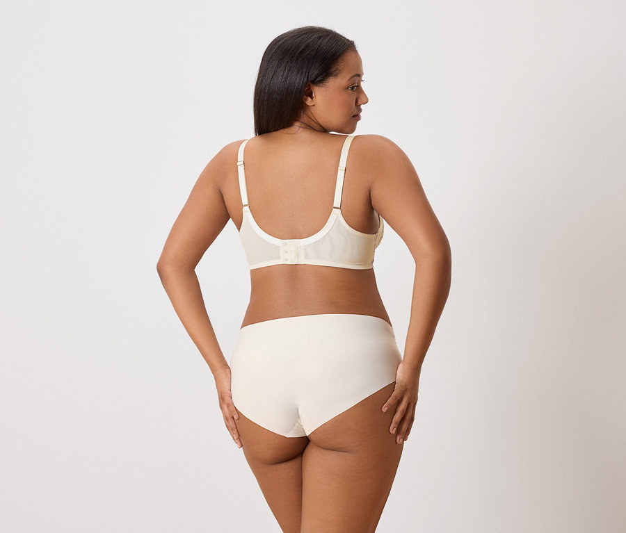 Femme à la peau foncée vue de dos, portant un soutien-gorge et une culotte blanc cassé.