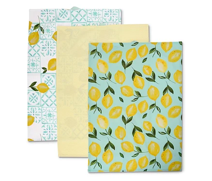 Trois torchons sont superposés : un avec un motif de citron sur fond bleu, un jaune, un avec un motif de carreaux bleus et blancs et un citron.