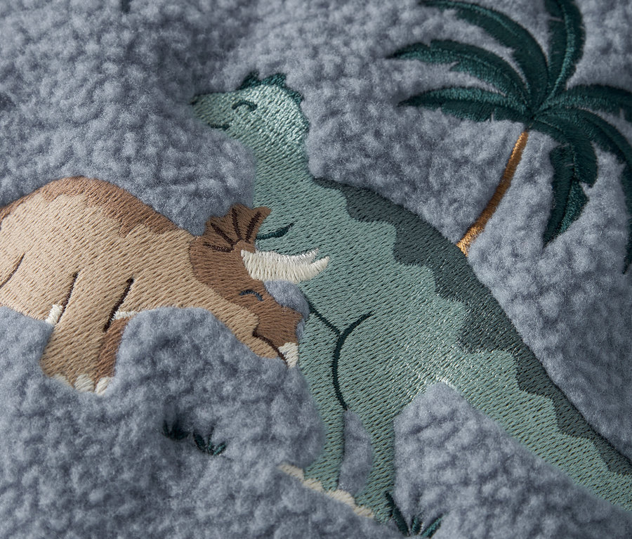 Gros plan sur un tissu gris avec des dinosaures brodés et un palmier.