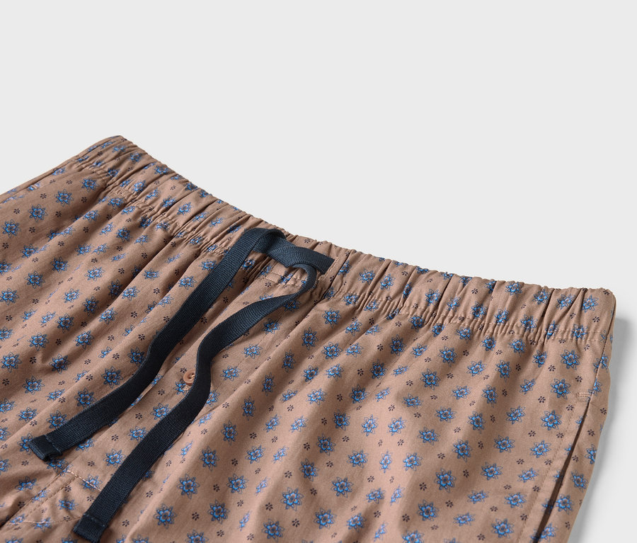 Gros plan d'un pantalon beige avec un motif floral bleu et un cordon de serrage bleu marine.