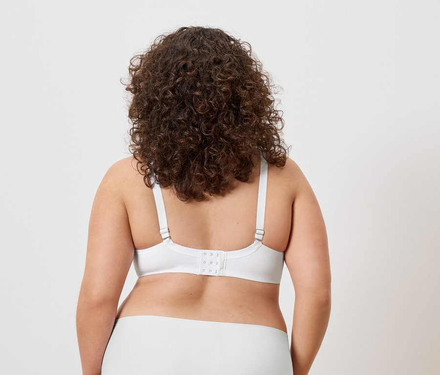Vue arrière d'une femme aux cheveux bouclés portant un soutien-gorge et une culotte blancs.