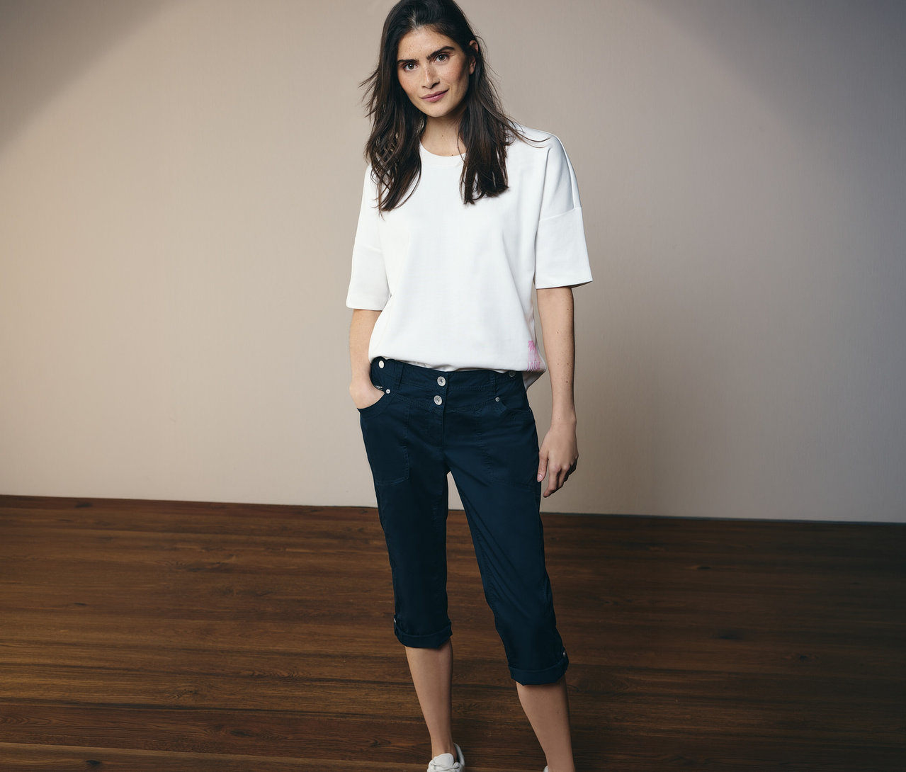 Femme portant un t-shirt blanc et un pantalon 3/4 Cecil «
New York
» bleu marine. Elle se tient sur un plancher en bois.
