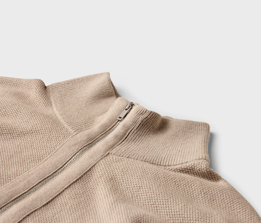 Gros plan d'un pull en tricot beige avec fermeture éclair et col montant.
