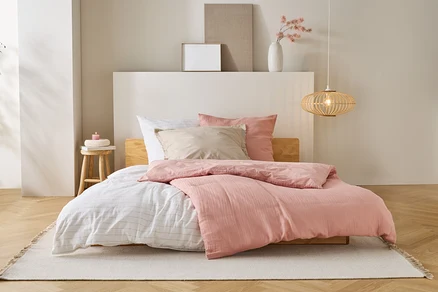 Un lit avec une couette rose, des draps blancs et des oreillers beiges se trouve sur un tapis dans une chambre.