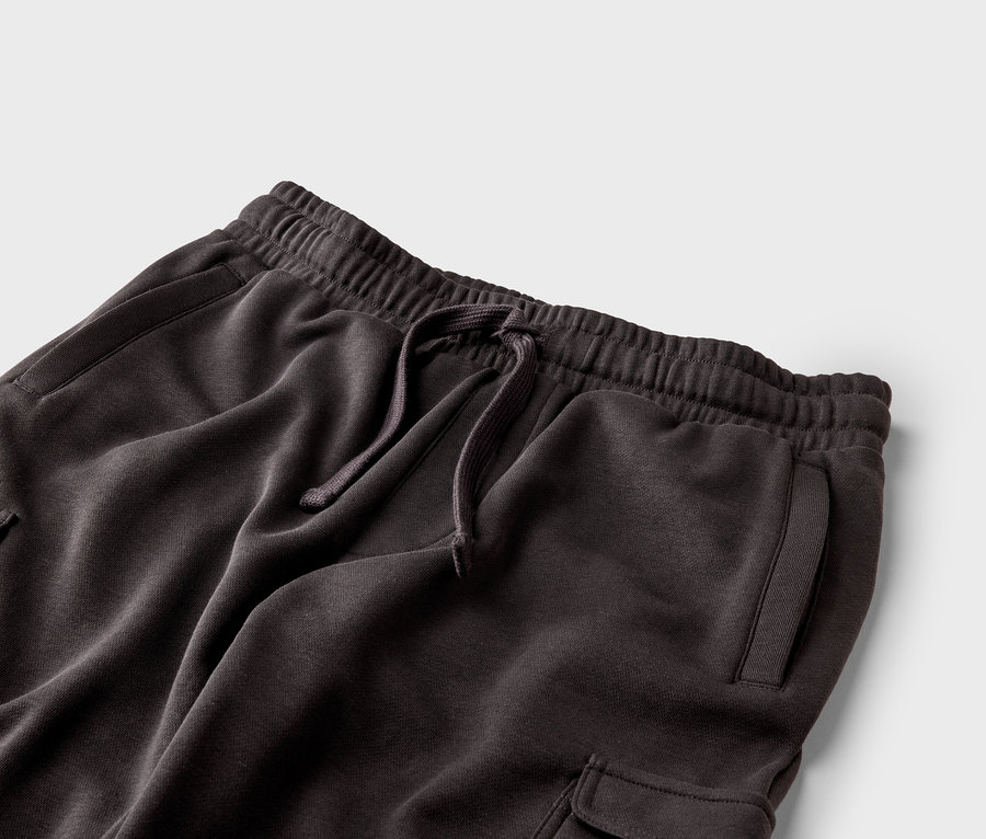 Gros plan d'un pantalon de jogging marron foncé avec cordon de serrage, taille élastique et poches sur fond gris.