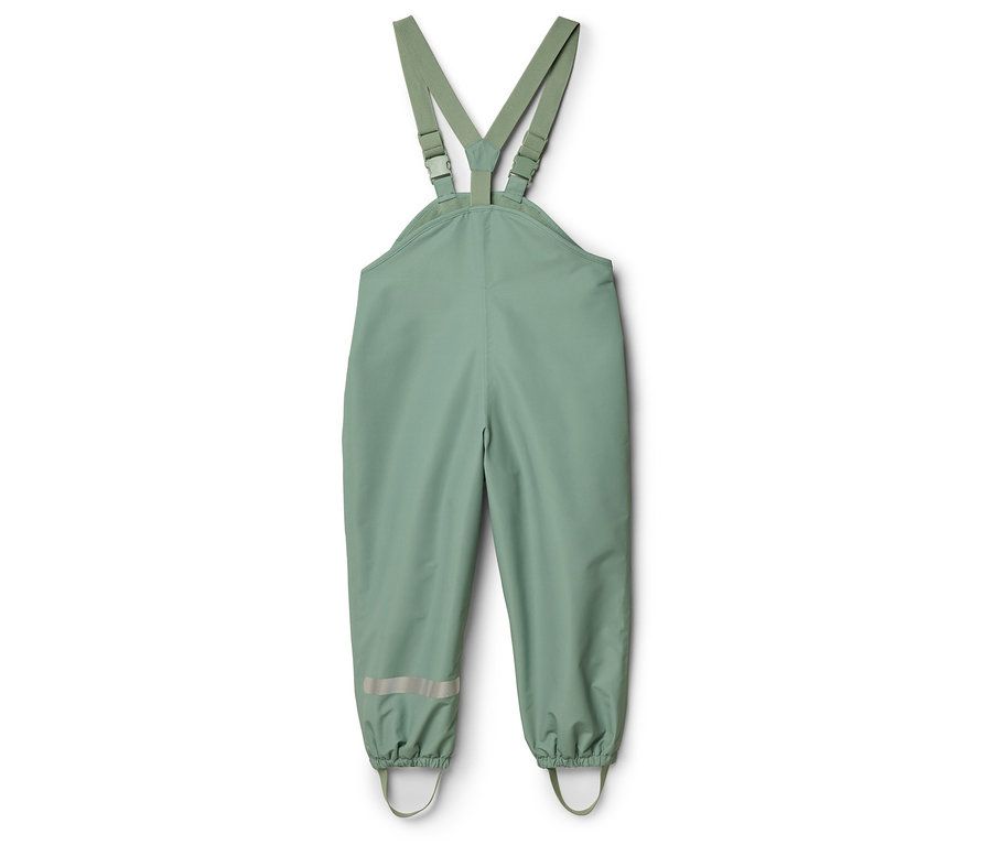 Un pantalon de pluie vert à bretelles est posé sur un fond blanc.