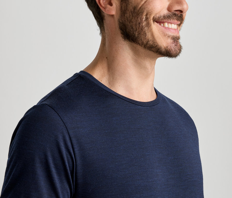 Gros plan d'un homme souriant avec une barbe, portant un t-shirt à manches longues bleu foncé.