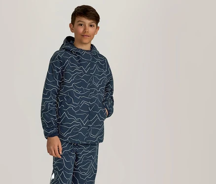 Un garçon se tient debout, une main dans la poche, portant un sweat à capuche bleu marine et un pantalon à motif zigzag blanc.