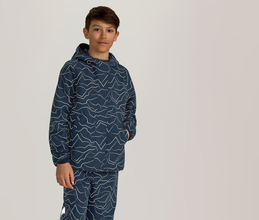 Un garçon se tient debout, une main dans la poche, portant un sweat à capuche bleu marine et un pantalon à motif zigzag blanc.