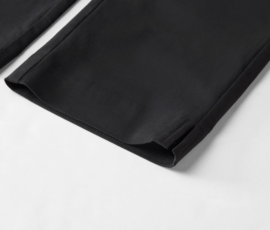 Gros plan sur le bas de pantalon noir avec fente à l'ourlet sur fond blanc.