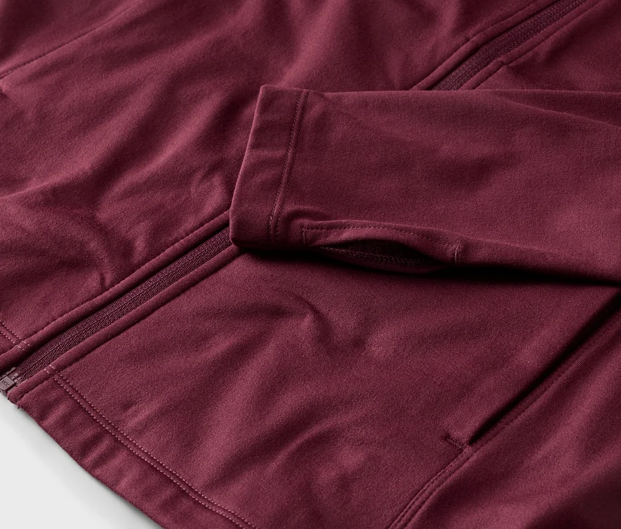 Gros plan sur une veste bordeaux avec fermeture éclair et trous pour les pouces.