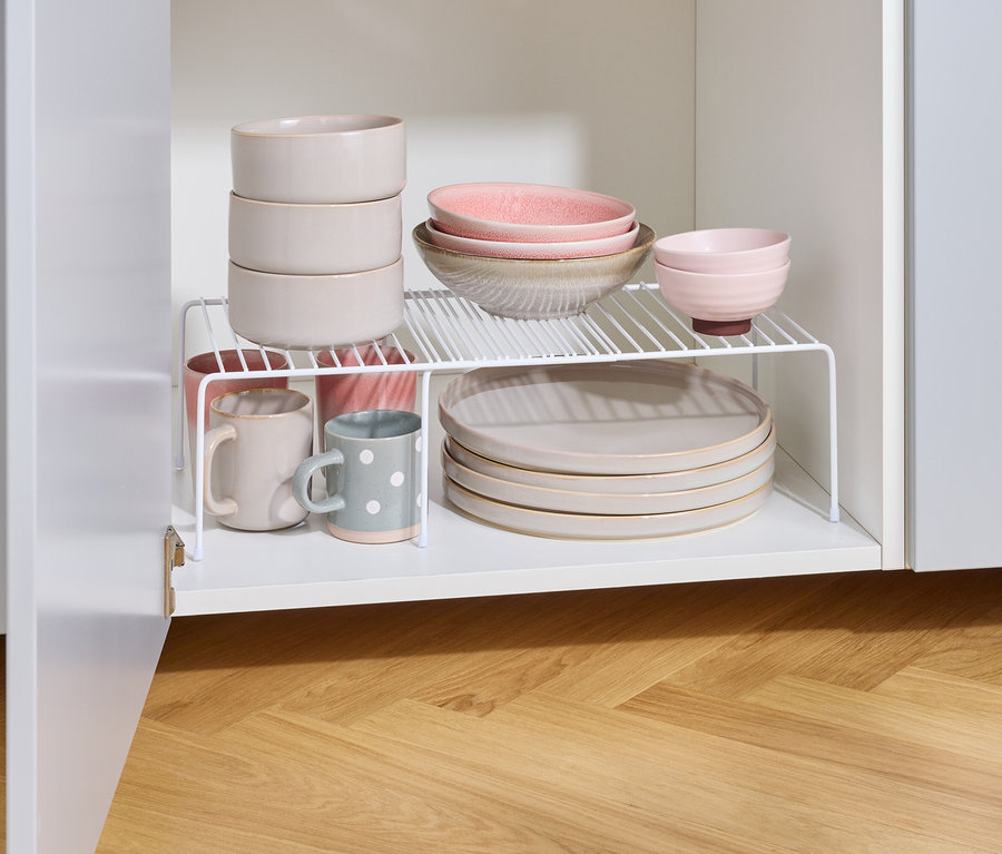 Dans l'armoire de cuisine, des assiettes, des bols et des tasses sont posés sur une étagère blanche.
