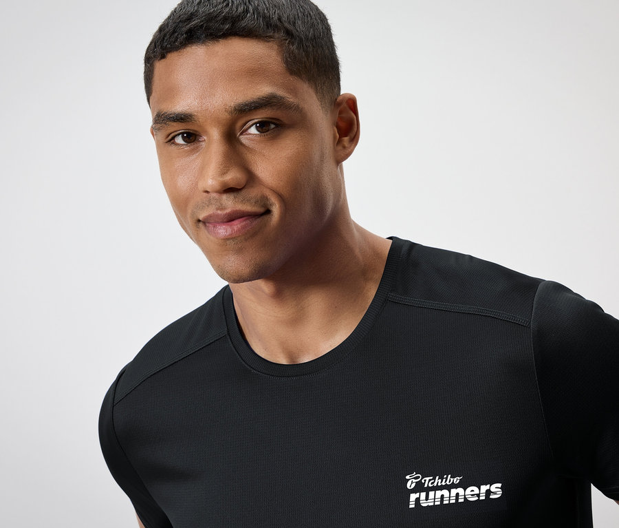 Un homme à la peau foncée porte un t-shirt noir avec l'inscription "Tchibo runners".