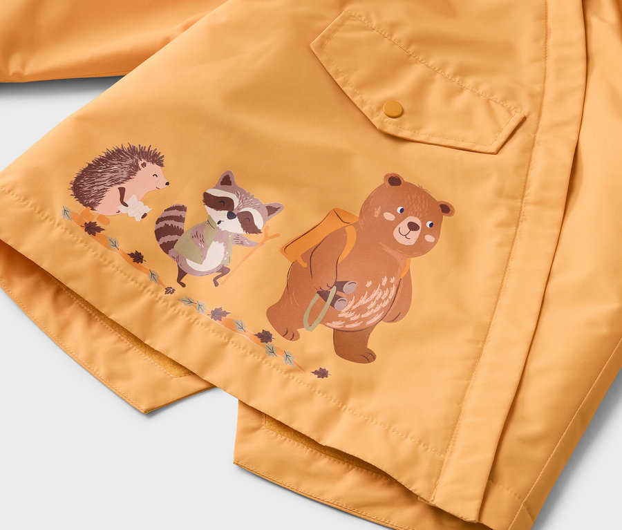 Gros plan d'une veste jaune avec un ours, un raton laveur et un hérisson imprimés, debout sur une branche.
