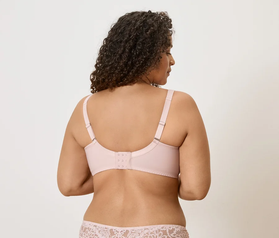 Vue arrière d'une femme aux cheveux bouclés portant un soutien-gorge rose clair et une culotte à motif de dentelle.